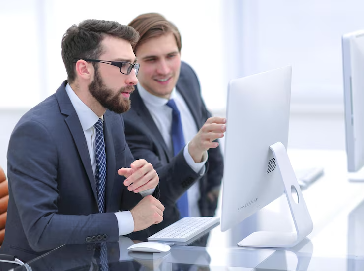 Two businessmen in suits collaborating at a computer in a bright office environment