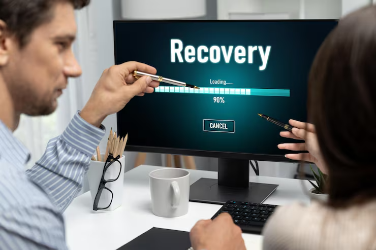 Two people discussing data recovery progress on a computer screen at 90% in an office setting
